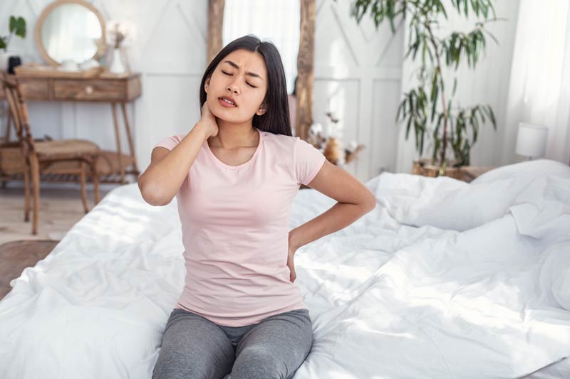 woman having pain in back and neck sitting in bed