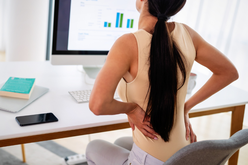 Woman Holding Back in Pain at Work Desk